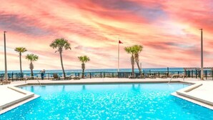 A swimming pool with a sunset view, palm trees, and a flag. - Sunbird 1BR/1BA, Direct Beachfront! Stunning Views! (Panama City Beach)