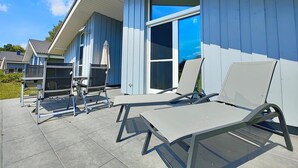 Un patio con mobiliario exterior, una zona de estar cubierta y un ventanal grande.
