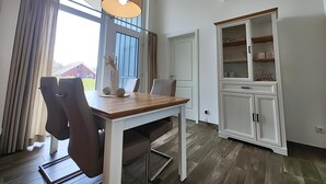 Un comedor con una mesa y sillas de madera, un colgante de luz y un armario blanco con estantes.