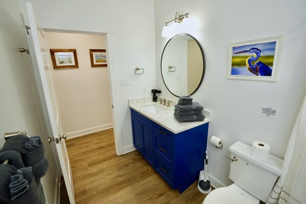 A bathroom with a white toilet, blue cabinets, a large mirror, and framed pictures on the wall.