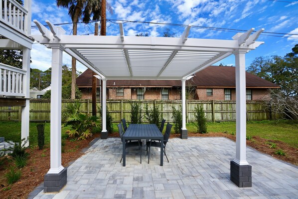 A covered patio with a table and chairs, surrounded by a brick patio and a wooden fence.