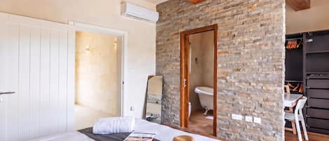 Un dormitorio con una cama grande, techo de madera, pared de piedra, baño con inodoro y lavamanos, y un armario.