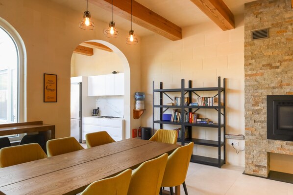 A dining area with a wooden table and yellow chairs, a bookshelf, and a fireplace.