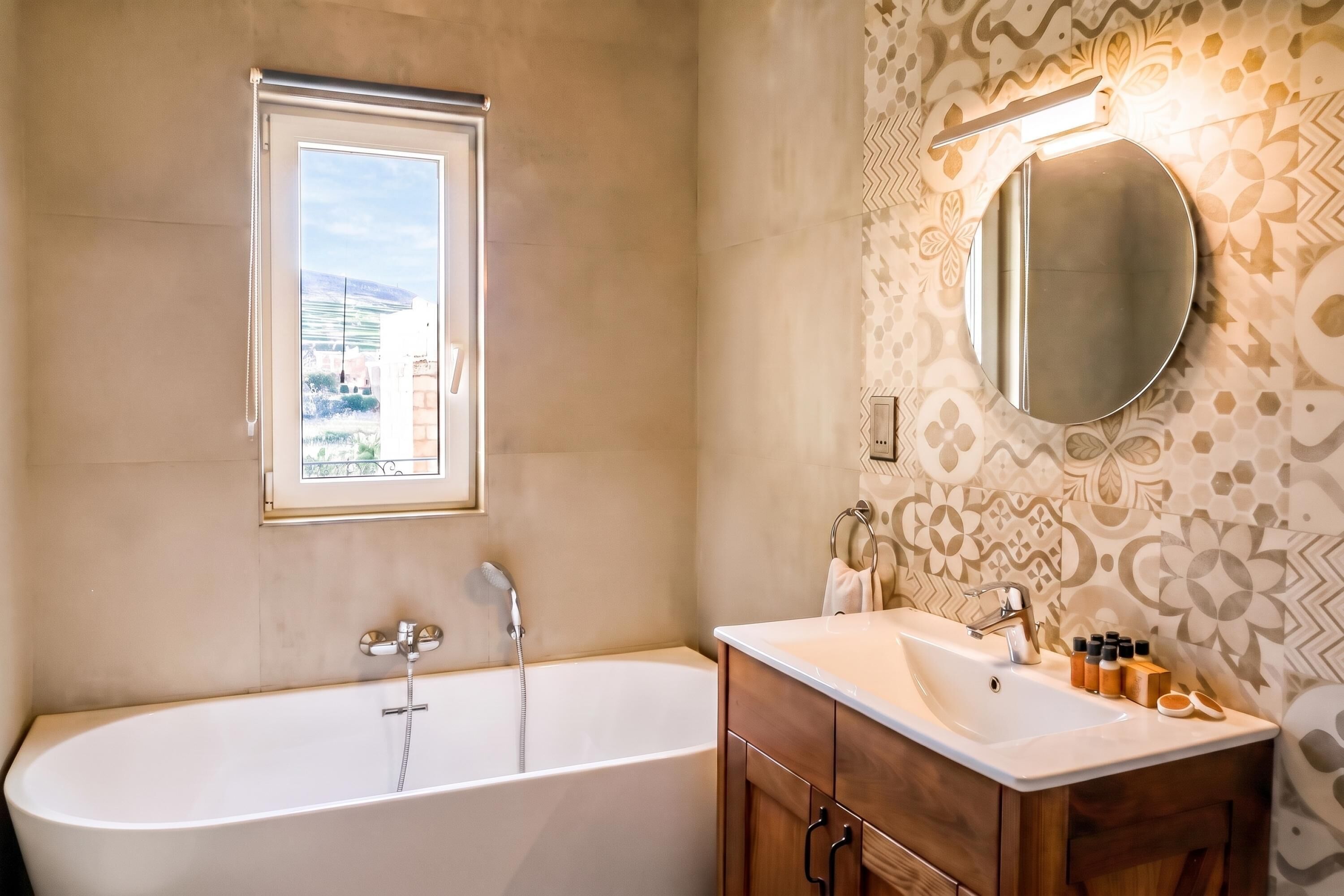 A bathroom with a freestanding bathtub, a vanity with a mirror, and patterned wall tiles.