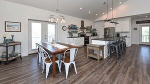 A spacious kitchen with white cabinets, a wooden dining table, and a bar area.