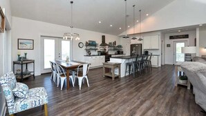 A spacious living area with a dining table, chairs, and a sofa. There is a kitchen area with cabinets and a refrigerator.