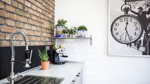 Et køkken med vask, kaffemaskine og plantet blomster på en hylde.