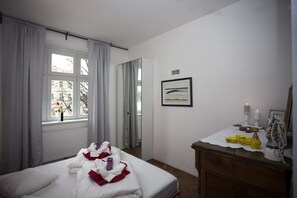 Ein Hotelzimmer mit einem Bett, einem Schminktisch, einem Fenster mit Vorhängen, einem gerahmten Bild an der Wand und einem kleinen Tisch mit Kerzen und Dekorationsgegenständen.