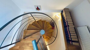 Un escalier en colimaçon avec des marches en bois et une rampe en métal, menant à l’étage supérieur.
