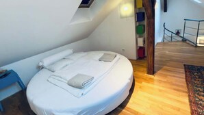 Un lit rond dans une chambre de style industriel, avec une lucarne, un plancher en bois et un petit escalier.