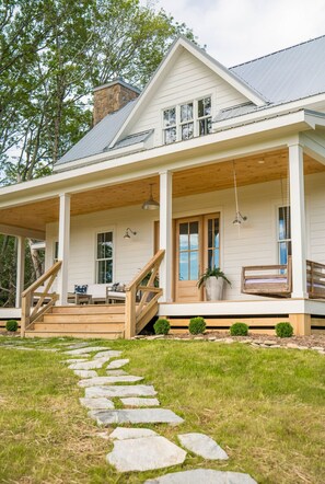 Een tweelaags huis met een overdekte veranda, stenen trappen die naar de ingang leiden en een kleine tuin.