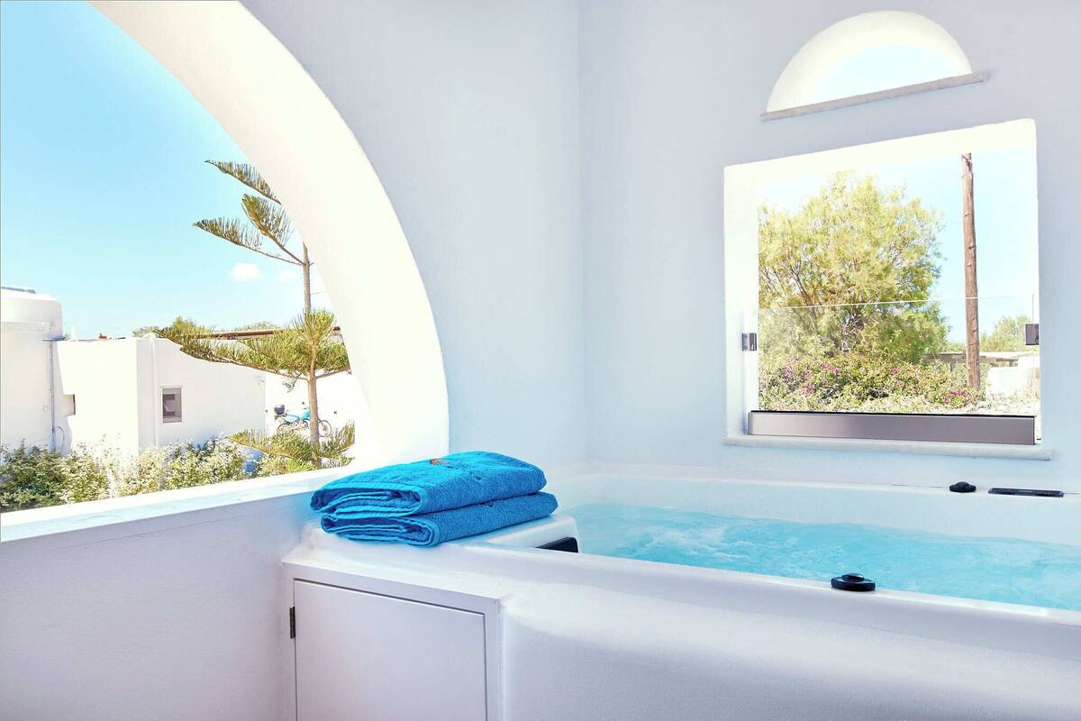 A modern bathroom with a bathtub, a window with a view of greenery, and a neatly folded towel on a counter.