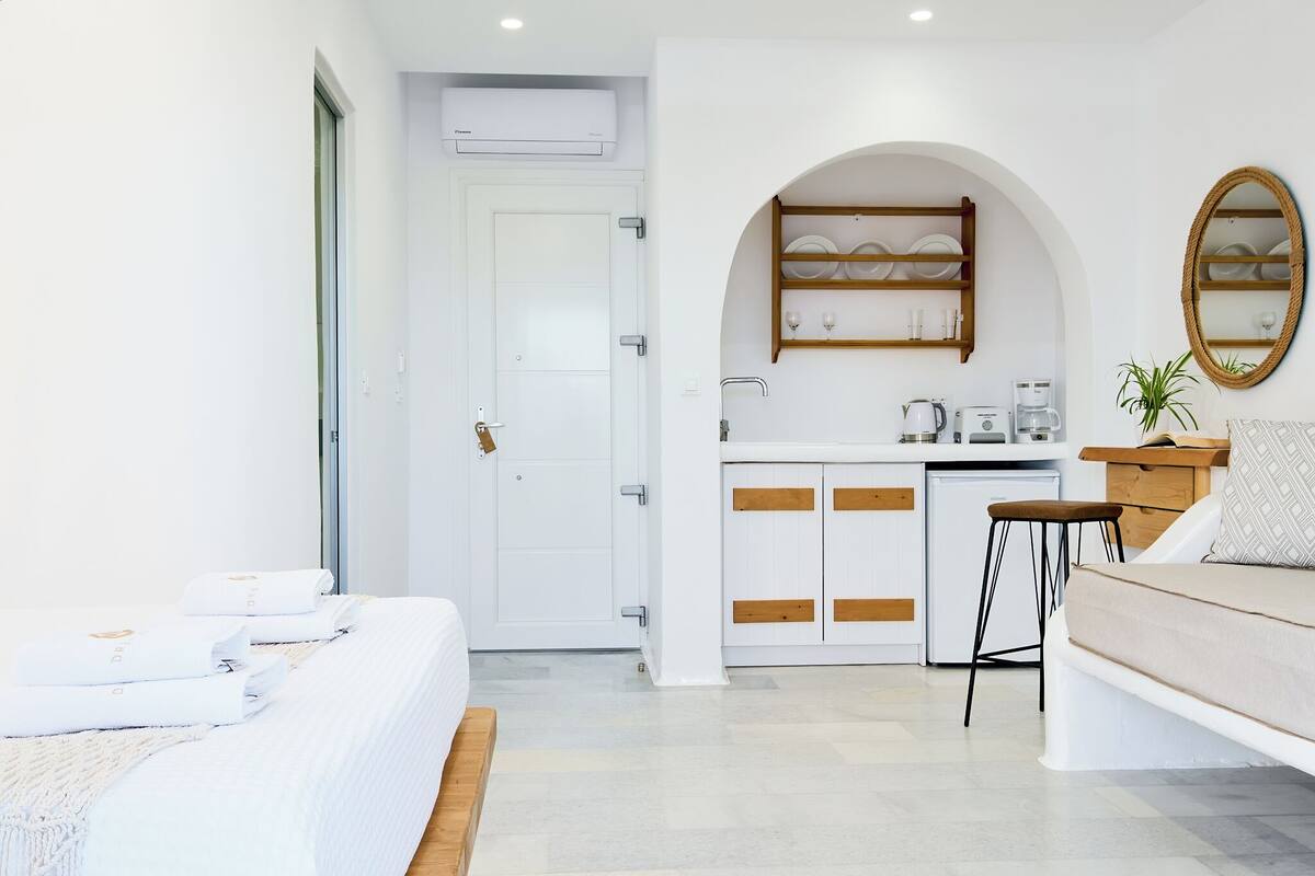 A modern hotel room with a bed, a sitting area, a kitchenette, and a bathroom.