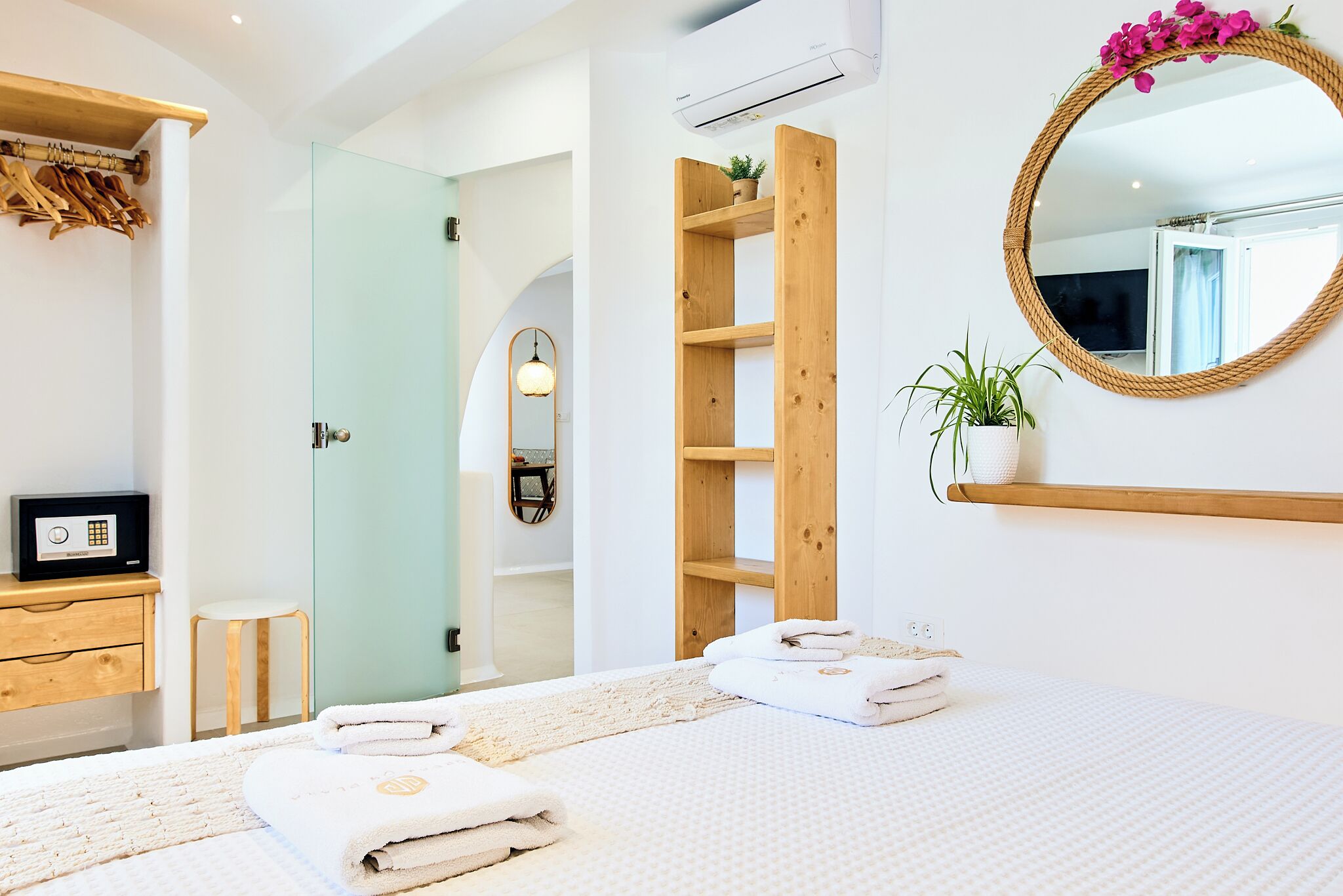 Un dormitorio moderno con una cama, un estante de madera con una planta, un espejo y una pequeña mesa con una silla.