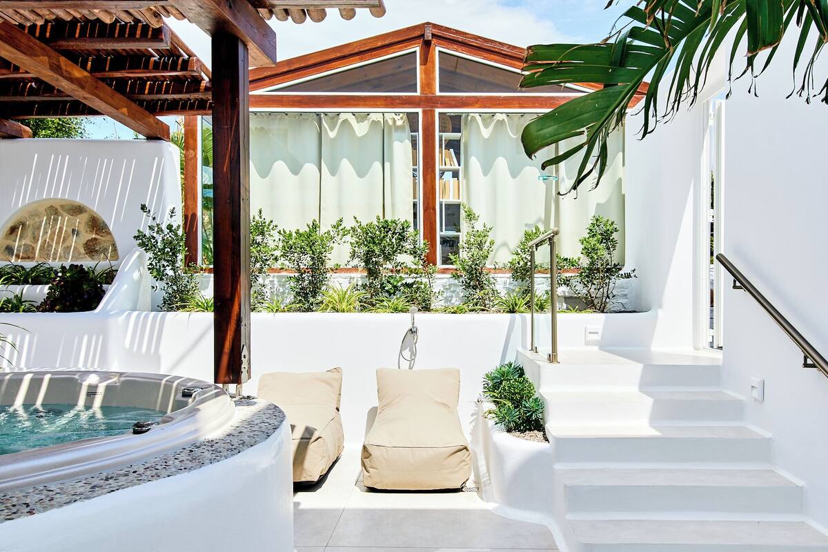 A rooftop terrace with a hot tub, two lounge chairs, and a staircase leading to an upper level.