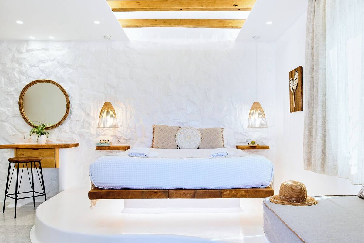 A modern bedroom with a large bed, bedside tables, a round mirror, and a wooden ceiling.