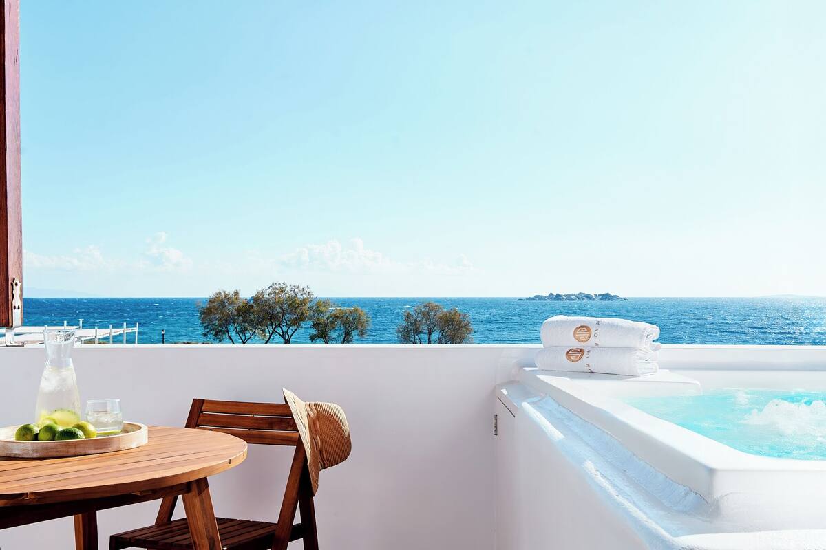 A balcony with a hot tub, a table with a drink, and a view of the sea.
