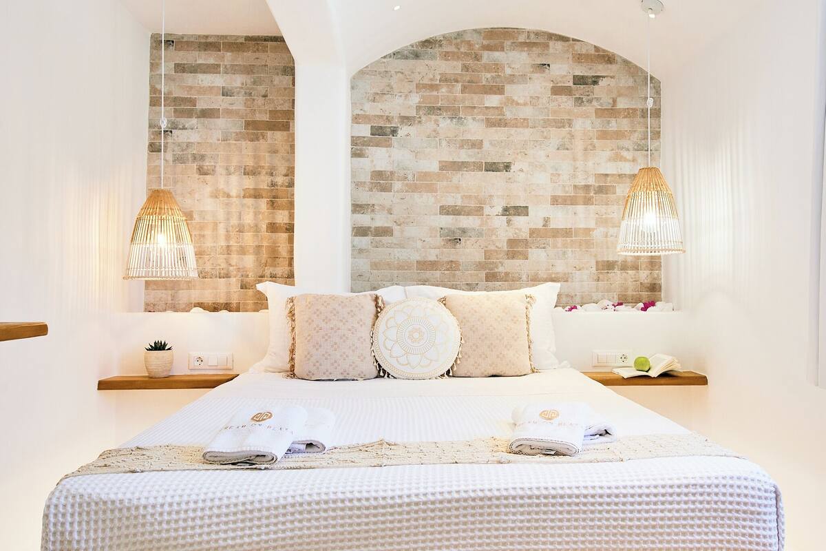 A hotel room with a large bed, two bedside tables, a brick wall, and two hanging lamps.