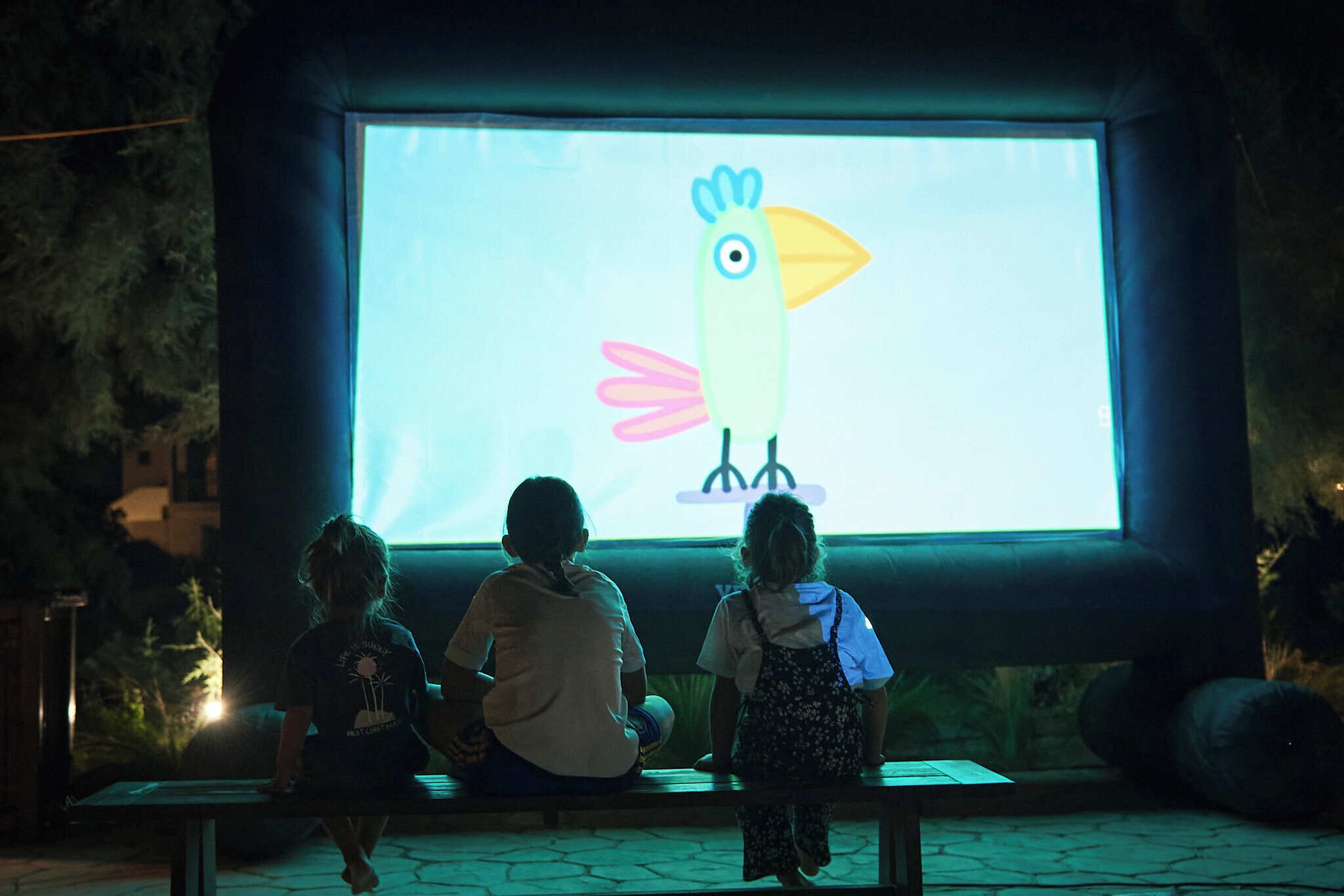 Une projection d’un oiseau aux couleurs vives sur un écran, avec deux personnes assises sur un banc devant.