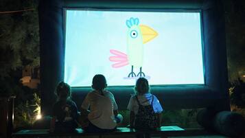 Une projection d’un oiseau aux couleurs vives sur un écran, avec deux personnes assises sur un banc devant.