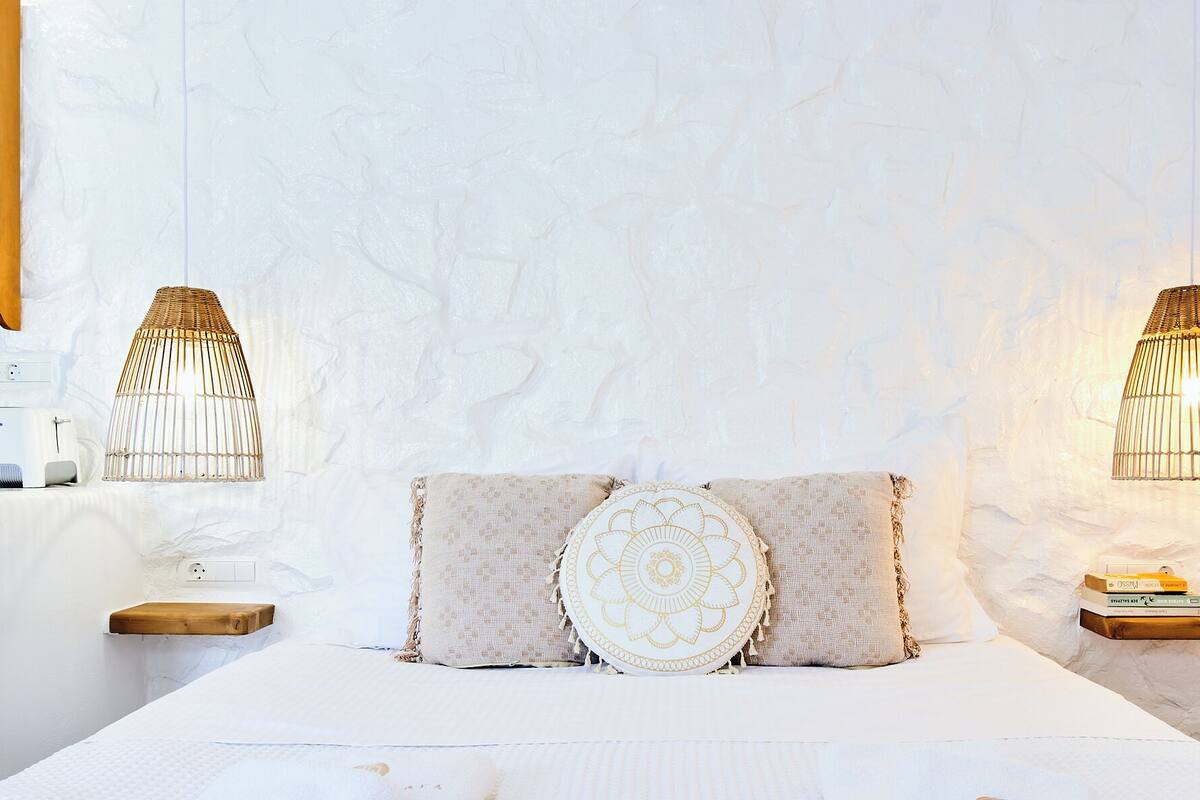 A bedroom with a bed, two bedside tables, a wall-mounted lamp, and a power outlet.