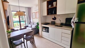 A modern kitchen with white cabinets, a built-in stove, and a sink. There is a dining area with a table and chairs. - Green Porto 06 (Ipojuca)