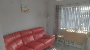 A red leather sofa, a small wooden table, a floor lamp, and a window with blinds. - 1br-garden-parking-pets-10 Mins to Beach (Hornsea)