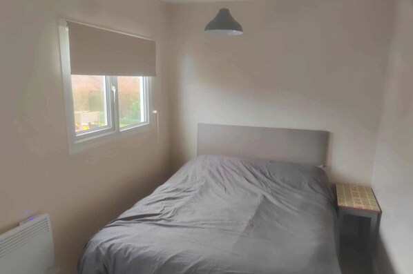 A bedroom with a single bed, a window with a blind, a bedside table, and a ceiling light fixture. - 1br-garden-parking-pets-10 Mins to Beach (Hornsea)
