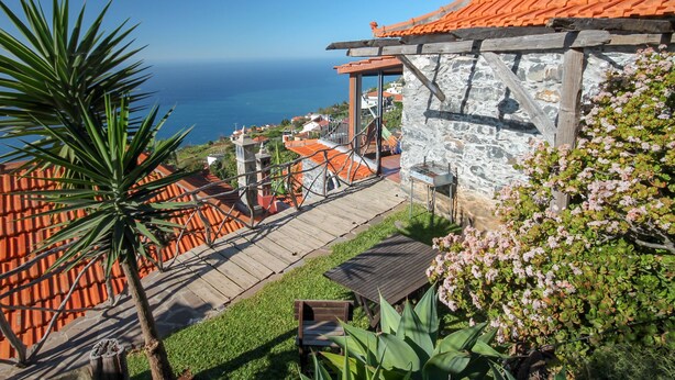 Una propiedad costera con un edificio de piedra, una terraza de madera y vistas al mar.