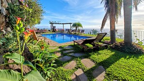 Un área de piscina con sillones de descanso, una pérgola y vistas al mar.