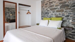 Un dormitorio con pared de piedra, cama con ropa blanca y cabecero de madera.