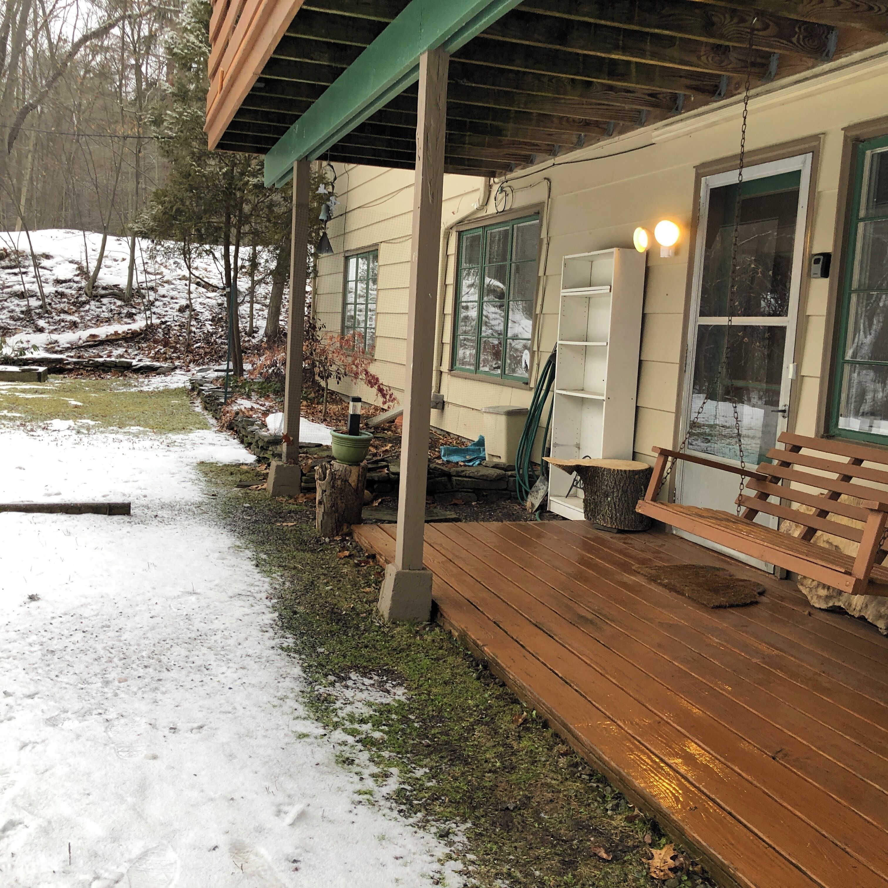 A wooden deck with a bench, a hanging light fixture, and a door with a window.