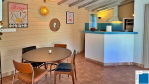 Un comedor con una mesa redonda y sillas, una cocina con encimera azul y un techo con vigas a la vista.