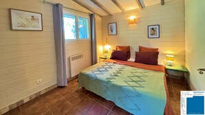 Un dormitorio con una cama, dos mesitas de noche con lámparas, una ventana con cortinas y un radiador.