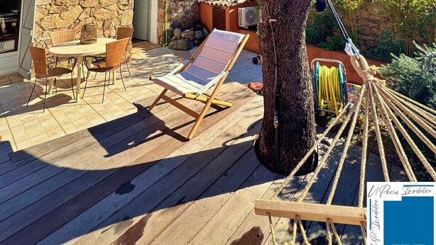 Una terraza de madera con una mesa y sillas, una hamaca y un edificio de piedra al fondo.