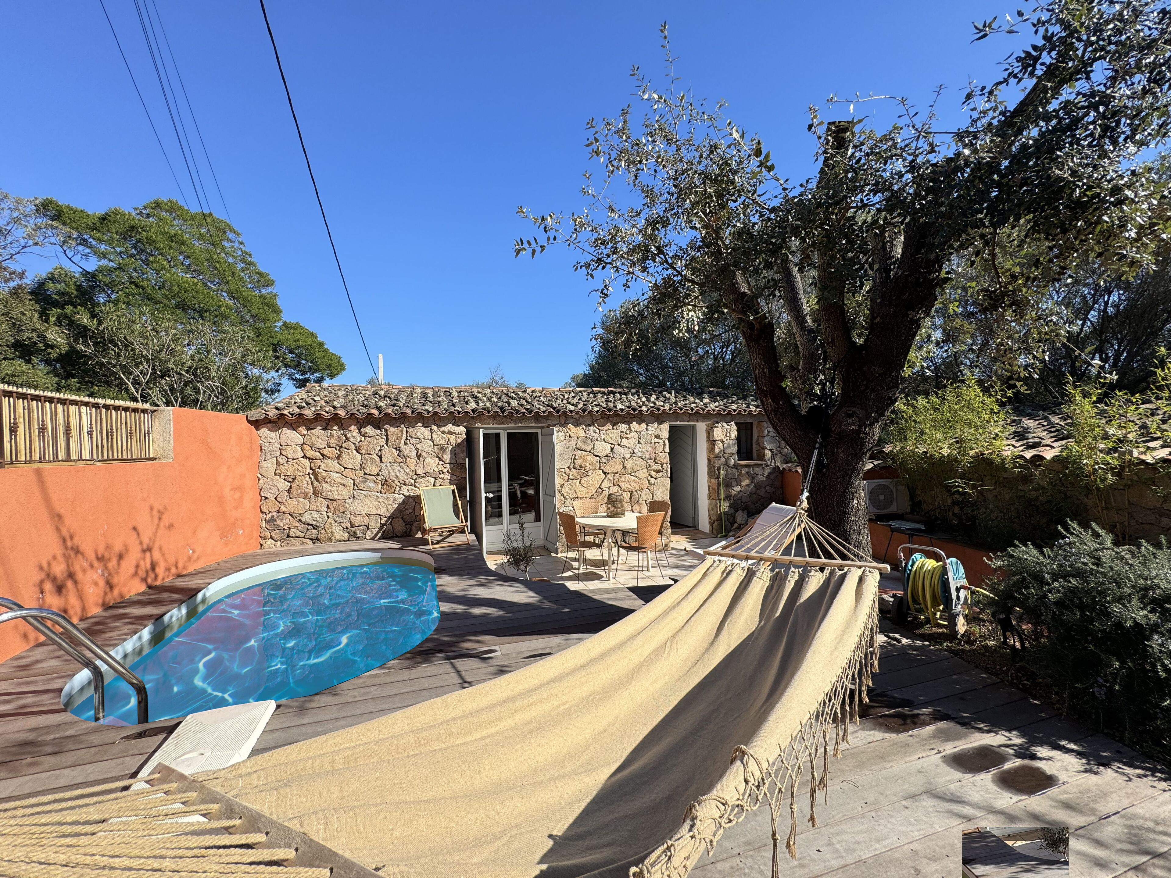 A pool area with a hammock, stone building, and outdoor furniture.