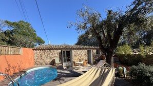 Un área de piscina con una hamaca, edificio de piedra y mobiliario exterior.