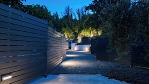 A pathway leading to a building with a modern design, surrounded by trees and a fence. - Rivière Residence Paros   (Paros)