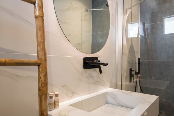 A modern bathroom with a marble vanity, a glass shower enclosure, and a wooden bath ladder. - Rivière Residence Paros (Paros)