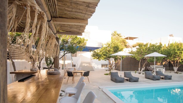 A poolside area with a wooden bar, white lounge chairs, and umbrellas. - Rivière Residence Paros   (Paros)