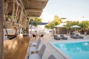 A poolside area with a wooden bar, white lounge chairs, and umbrellas. - Rivière Residence Paros (Paros)