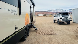 A white RV with "RV SUITE" written on it, parked in a dry, open area with mountains in the background. - 4,000 sq.ft. Jeep Shop Man Cave with Luxury Trailer (Moab)