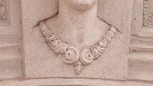Detallada talla de piedra que representa una figura con alas y tocado, probablemente parte de la arquitectura de un edificio.
