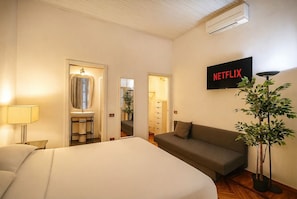 Une chambre d’hôtel avec un lit, un canapé, un téléviseur affichant le logo « NETFLIX », une plante et un miroir.