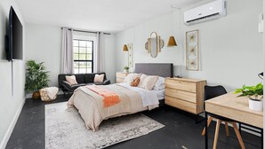 Ein modernes Schlafzimmer mit Bett, Nachttischen, Schreibtisch, Stuhl, Fernseher und Klimaanlage.