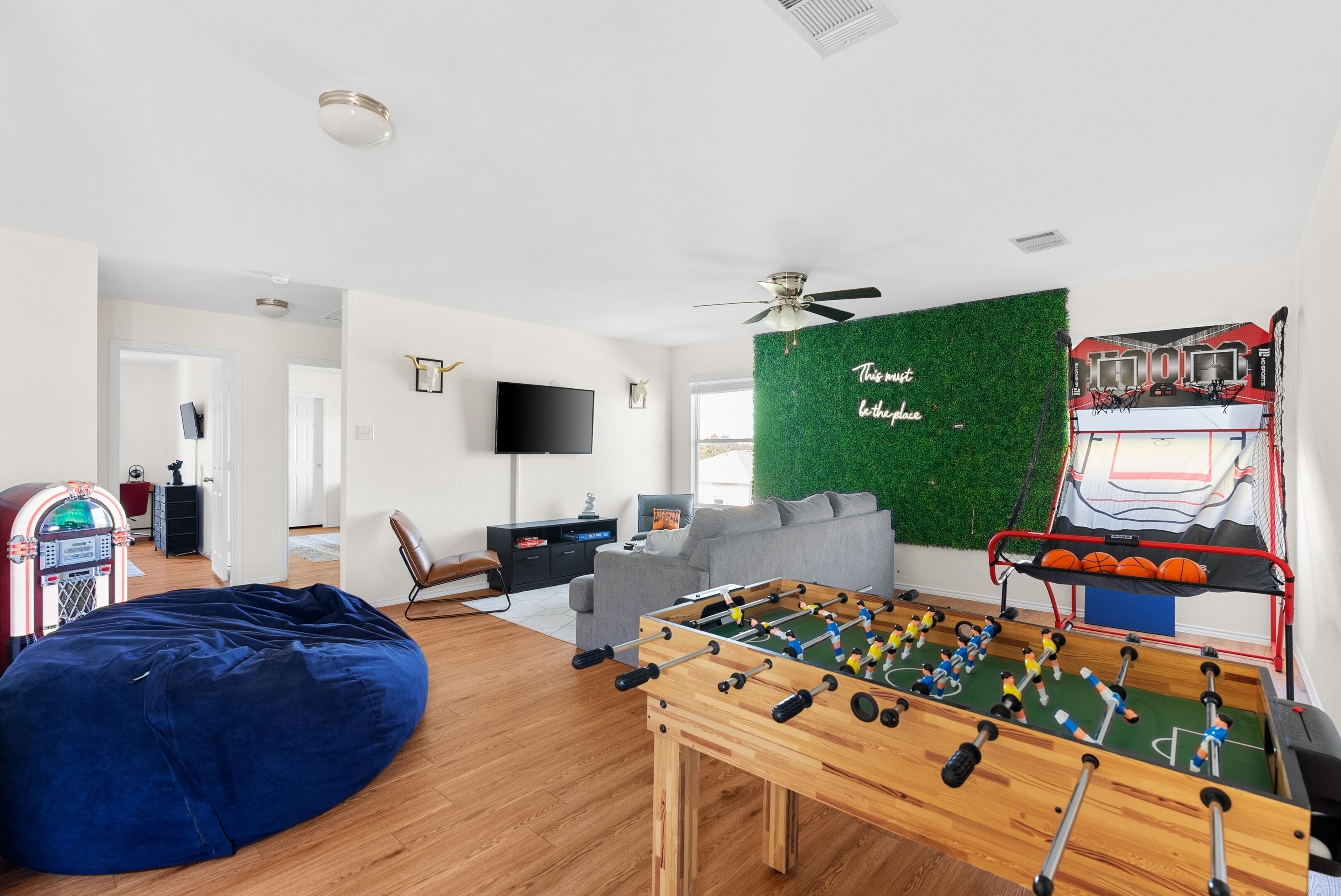 Een woonkamer met een tafelvoetbaltafel, een blauwe pluchen zitzak, een televisie en een groene wand met een basketballen.