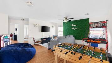 Een woonkamer met een tafelvoetbaltafel, een blauwe pluchen zitzak, een televisie en een groene wand met een basketballen.
