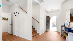 Um corredor espaçoso com piso de madeira, uma escada e uma porta que dá para o exterior.