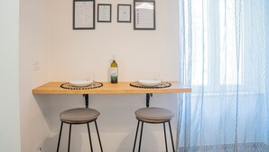 A kitchen area with a wooden table, two bar stools, a bottle of wine, and framed certificates on the wall.