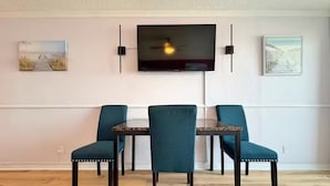 A dining area with a table and four chairs, a flat-screen TV mounted on the wall, and two framed artworks on either side. - The Lidiya Room, right on the famous Daytona Beach. (Daytona Beach)
